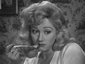 Liz Fraser with wavy blonde hair and wearing a white shirt while holding a spoon.