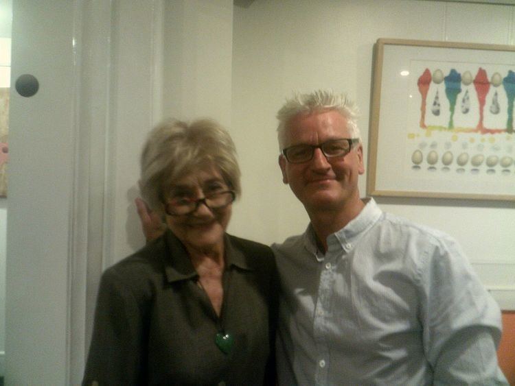 Liz Fraser wearing eyeglasses and a dark-green blouse with a man wearing eyeglasses and white long sleeves.