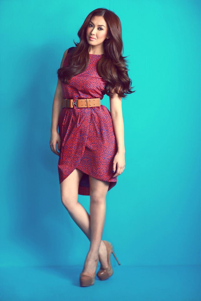 Liz Uy with long wavy hair, wearing a red dress, brown belt, and brown heels.