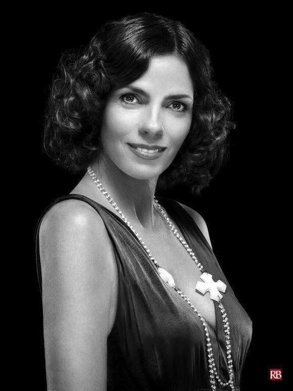 Élizabeth Bourgine smiling with curly hair and wearing a sleeveless v-neck dress exposing her cleavage and a bead necklace