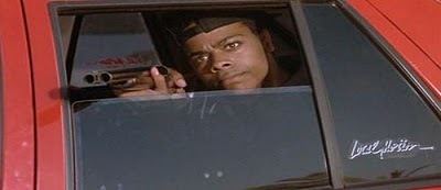 Scene from Boyz n the Hood movie, featuring Lloyd Avery II wearing a black cap and holding a gun inside a red car.