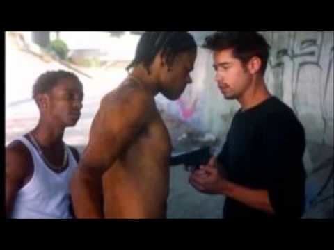 A man wearing a black shirt and pointing a gun at Lloyd Avery II with a man wearing a white sleeveless shirt.