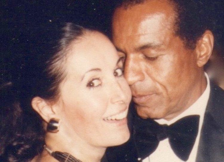 Carolyn Haynes smiling while Lloyd-Haynes is beside her wearing a black coat, white long sleeves, and black bow tie