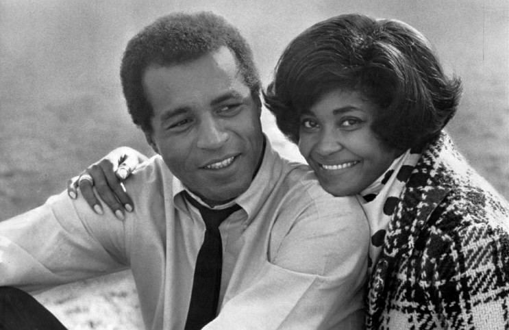 Lloyd Haynes smiling and wearing long sleeves and a necktie while Nancy Wilson wearing a checkered coat and polka dot scarf
