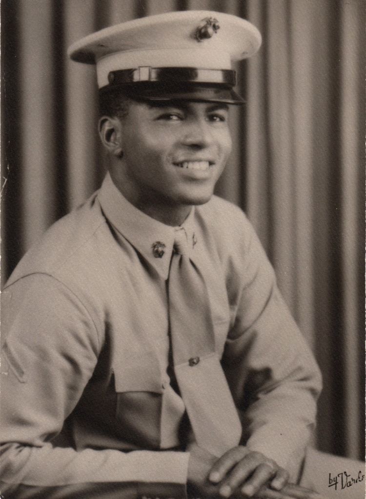 Lloyd Haynes smiling while wearing a peaked cap, long sleeves, and necktie
