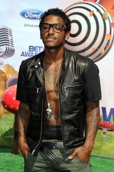 Lloyd posing at the BET Awards with his tattoos visible and wearing a black leather jacket as well as eyeglasses and a necklace.
