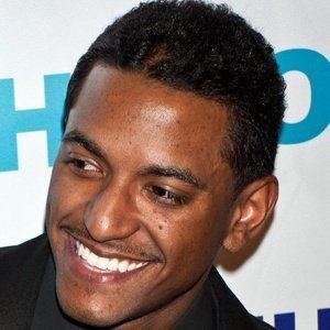 Lloyd Polite Jr. smiling at an event and wearing a black suit and tie.