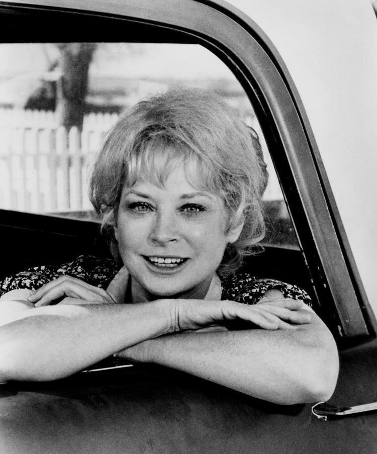 Lois Nettleton smiling while her arms are leaning on the car window and she is wearing a blouse