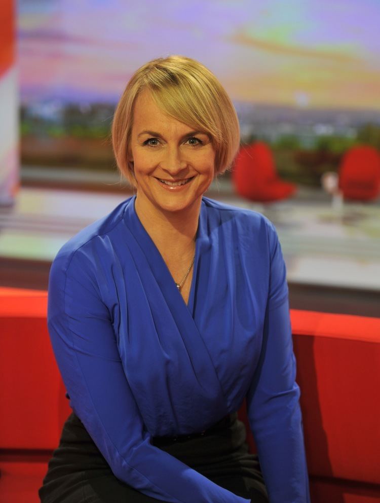 Louise Minchin smiling while wearing a blue long sleeves blouse and black skirt