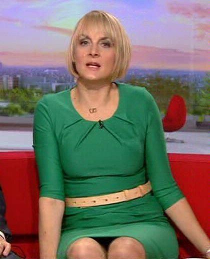 Louise Minchin sitting on a red couch while wearing a green dress and gold belt