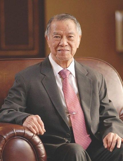 Lucio Tan sitting on a couch while wearing black coat, white long sleeves and neck tie