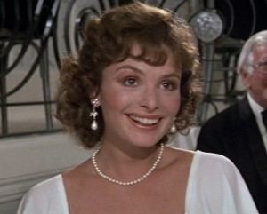 Lucy Gutteridge smiling while wearing a white blouse, pearl necklace, and earrings in a scene from the 1984 film, Top Secret!