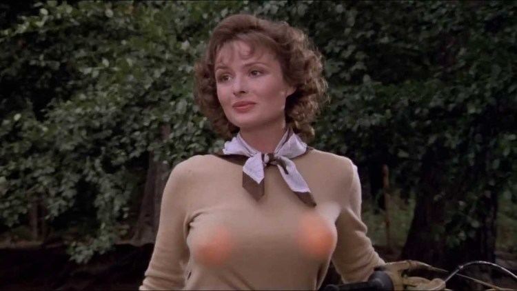Lucy Gutteridge with a tight-lipped smile while wearing a beige long sleeve blouse and ribbon scarf in a scene from the 1984 film, Top Secret!