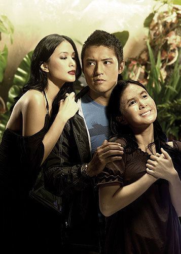 The movie poster of Luna Mystika 2008, in a Enchanted forest at the back, from left, Heart Evangelista is serious, standing, leaning to Mark’s shoulder with her right hand, has long black hair wearing a black noodle strap dress, in the middle, Mark Evangelista is serious, standing holding Heart (right) shoulder, looking to his right, has black hair wearing a blue shirt under a black jacket and a watch, at the right, Heart Evangelista is smiling, leaning back, with her hands on her chest together, has long black hair wearing a brown long blouse.