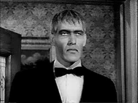 Lurch (The Addams Family) looking annoyed while inside a room wearing a shirt, a bow tie, and a coat