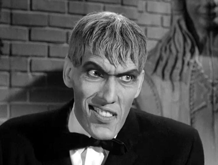Lurch (The Addams Family) with his scary look while wearing a white shirt, a bow tie, and a coat
