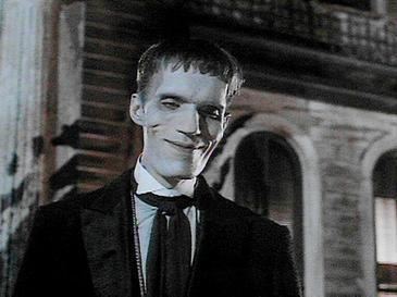 Lurch (The Addams Family) smiles outdoors while wearing a white shirt and a black coat