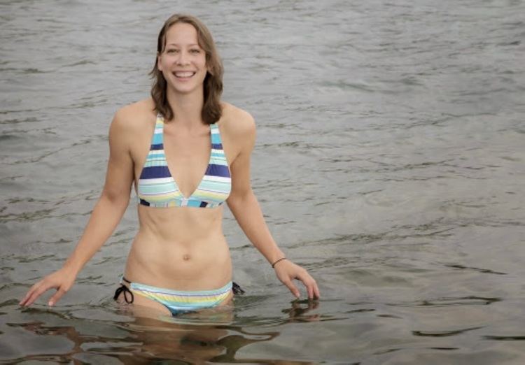 Luria Petrucci smiling while wearing a blue striped bikini at the beach
