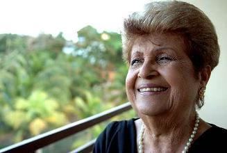 Lydia Echevarría smiling while wearing a black blouse, earrings, and pearl necklace