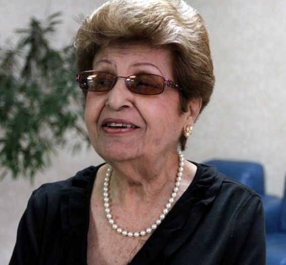 Lydia Echevarria talking to someone while wearing a black blouse, pearl necklace, earrings, and sunglasses