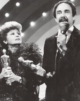 Luis Vigoreaux giving a speech and he is wearing a coat, long sleeve, and necktie while Lydia Echevarría looking at him