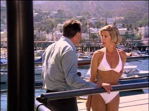 Lynette Mettey with short blonde hair and wearing a white swimsuit talking with a man wearing long sleeves and pants.