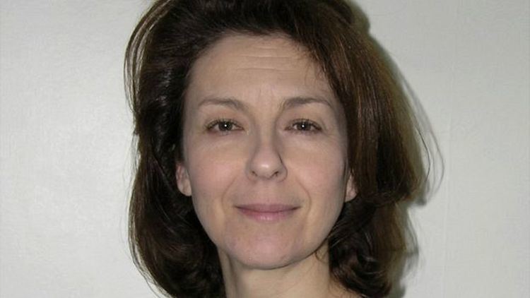 Lynn Bowles with a tight-lipped smile and shoulder-length wavy hair.