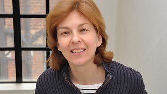 Lynn Bowles smiling, with wavy blonde hair and wearing a gray knitted jacket over a white and black shirt.