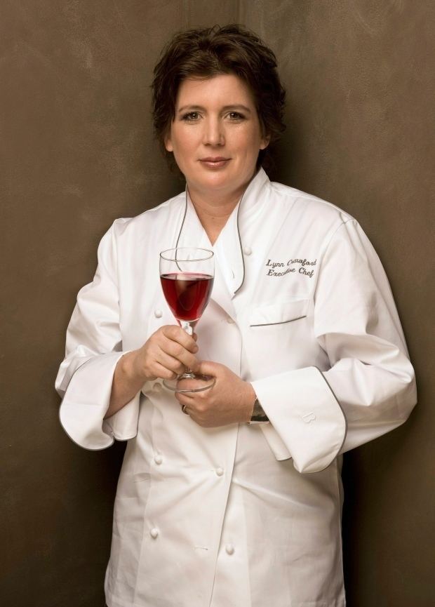 Lynn Crawford smiling and holding a goblet while wearing white chef's uniform
