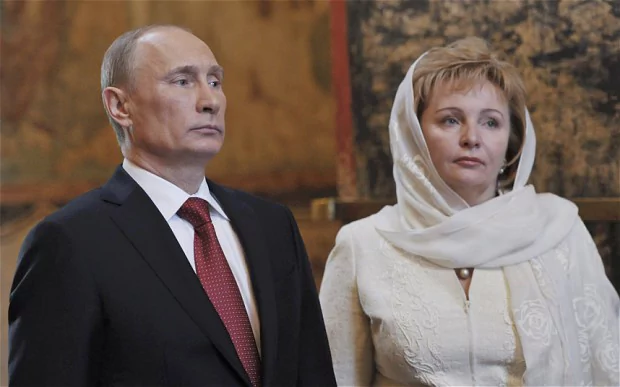 Vladimir Putin and Lyudmila Putina are looking afar with serious faces. Vladimir is wearing a black coat, white long sleeves, and maroon necktie while Lyudmila is wearing a white blouse and hijab