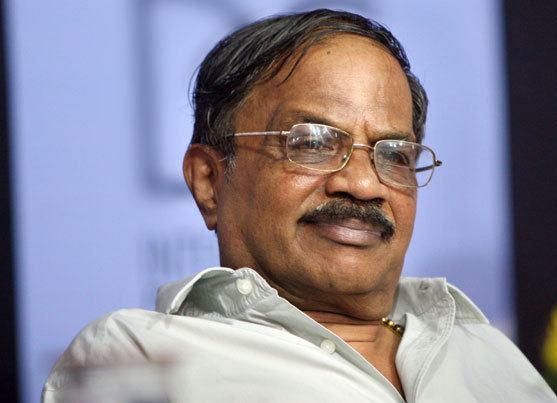 M. T. Vasudevan Nair in an event wearing a white polo shirt along with a bead necklace and eyeglasses.
