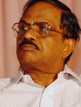 M. T. Vasudevan Nair looking at something and wearing a striped polo shirt along with red eyeglasses.