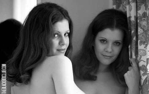 The Collinson twins, Madeleine and Mary Collinson, are smiling in both images, the first identical twin Playmates in Playboy Magazine. The one on the left is facing back, has long hair, and is naked. The other on the right is holding on to a floral curtain with a mirror in the background, has long hair, and is naked.