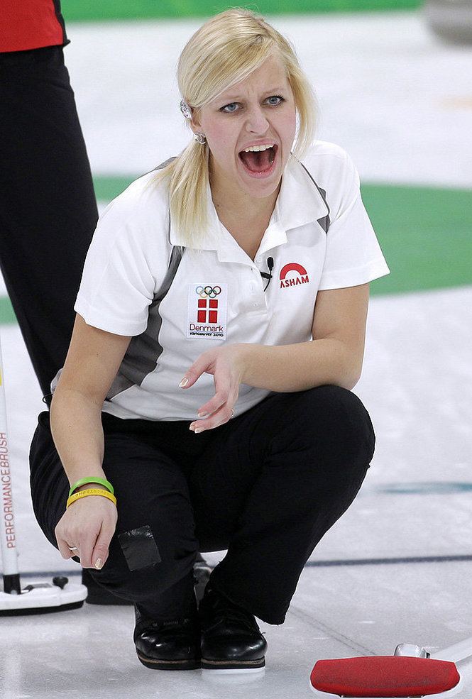 Madeleine Dupont shouting while sitting on the floor and wearing black pants, curling shoes, and a white T shirt with red and gray print