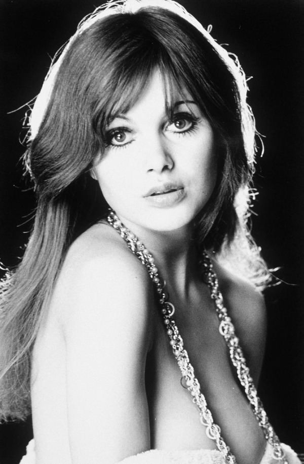 Madeline Smith wearing a long necklace and blouse showing her cleavage