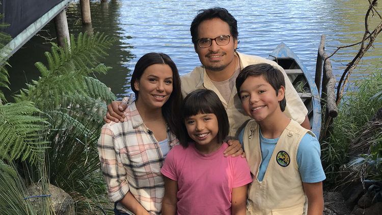 Madelyn Miranda as Young Dora with her co-stars, Michael Peña, Eva Longoria, and Malachi Barton in Dora and the Lost City of Gold movie. Madelyn smiling and wearing a pink shirt.