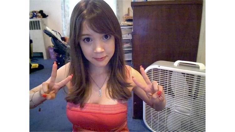 Magibon with a tight-lipped smile while doing the peace sign and wearing an orange sleeveless blouse and necklace