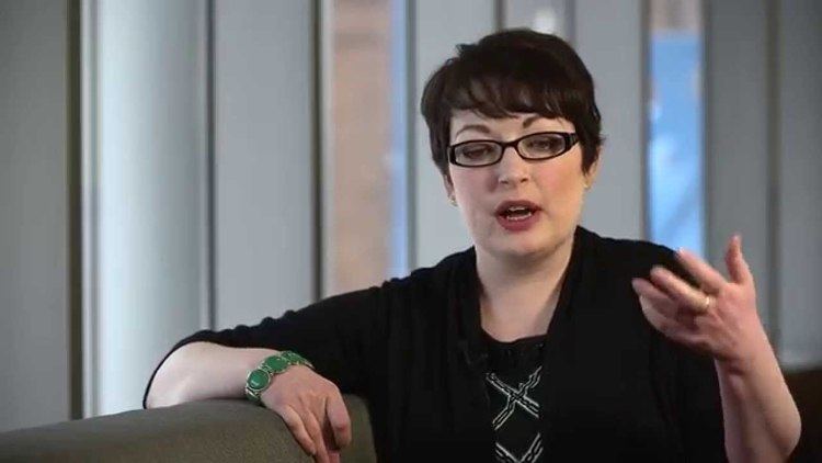 Mahtob Mahmoody speaking with hand gestures while wearing a black blouse, eyeglasses, and green bracelet