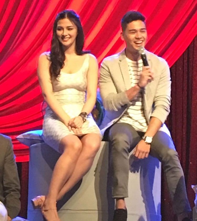 Maika Rivera smiling and wearing white mini dress while Marco Gumabao sitting next to her
