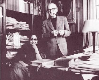 Maitreyi Devi smiling while Mircea Eliade smoking in the library and wearing a coat and long sleeves