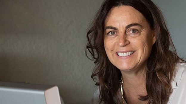 Maja Hoffmann smiling, with wavy hair, wearing a necklace, and a white blouse.