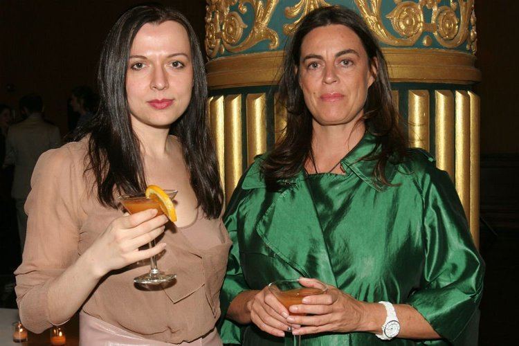 Maja Hoffmann and Vlatka Horvat holding a cocktail glass. Maja with a serious face, messy hair, and wearing a green dress while Vlatka Horvat is with a serious face and wearing a brown dress.