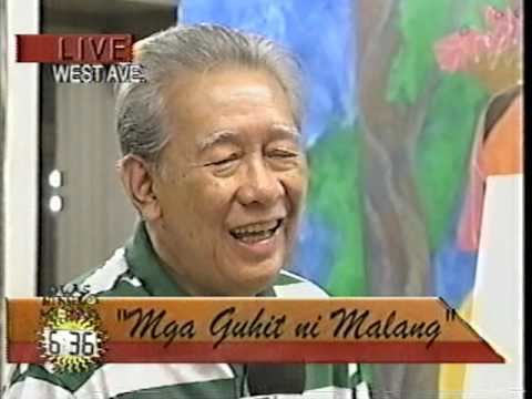 Malang smiling while being featured in a show with a Filipino caption and English translation "Arts by Malang". Malang has gray hair and wearing a shirt with green and white stripes with a tree painting in his background