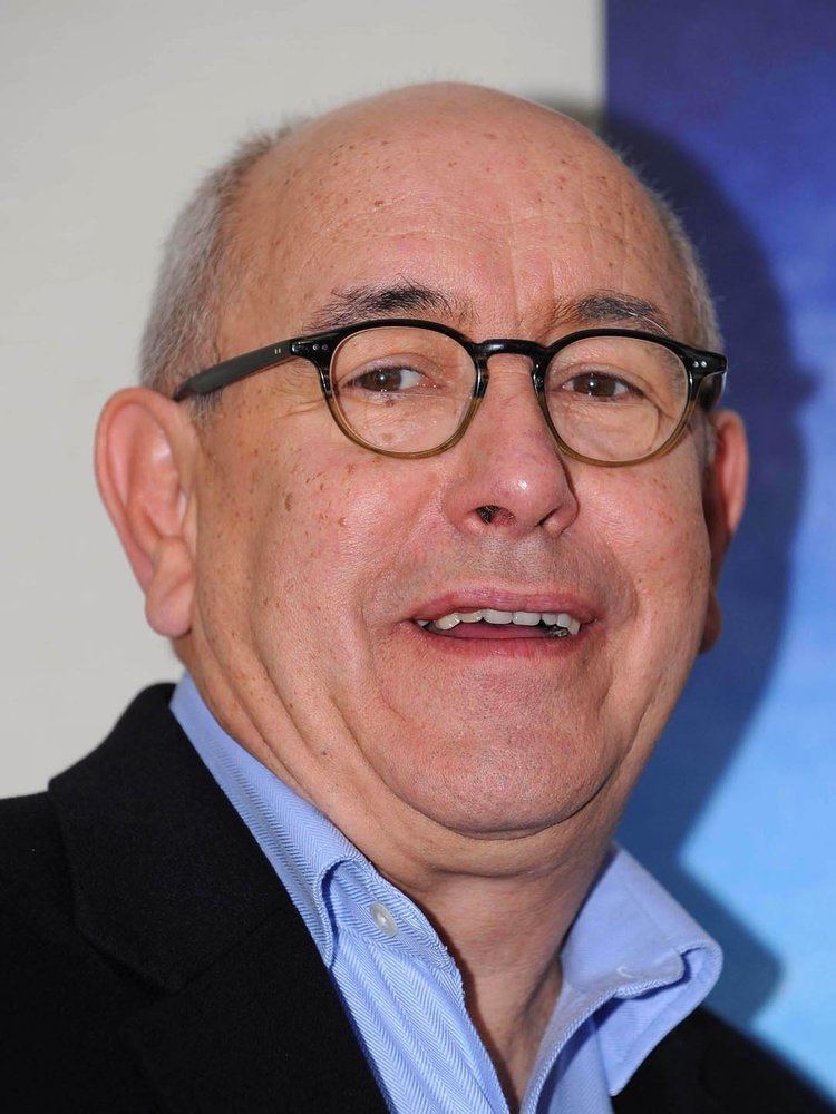 Malcolm Hebden smiling and wearing glasses and a suit over his clothes.