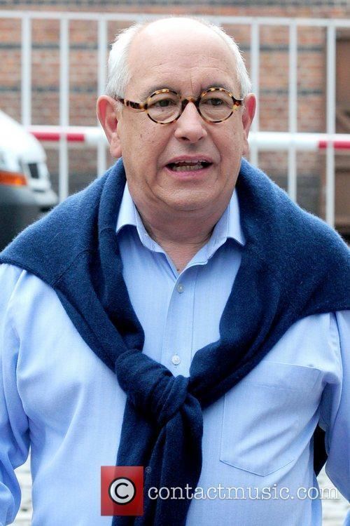 Malcolm Hebden arriving at a movie set and wearing glasses as well as a sky blue long-sleeve and a blue scarf.