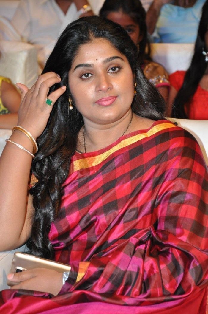 Mamilla Shailaja Priya fixing her hair in a gathering and holding her wallet while wearing a strped red dress.