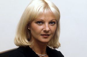 Mandy Rice-Davies posing with short white hair and wearing a gold necklace and black dress.