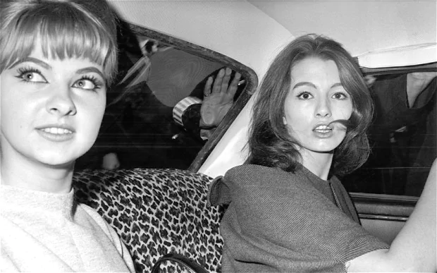 Mandy Rice-Davies inside a car with Christine Keeler looking at fans from the outside.