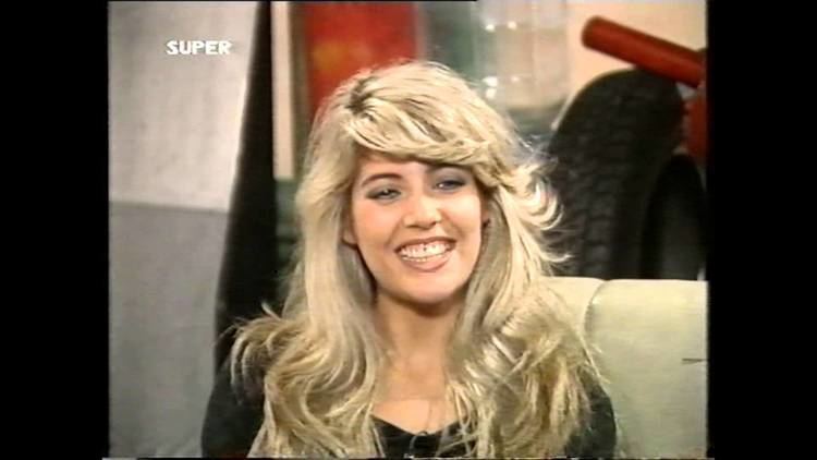 Mandy Smith smiling while sitting on the couch during an interview and wearing a black blouse