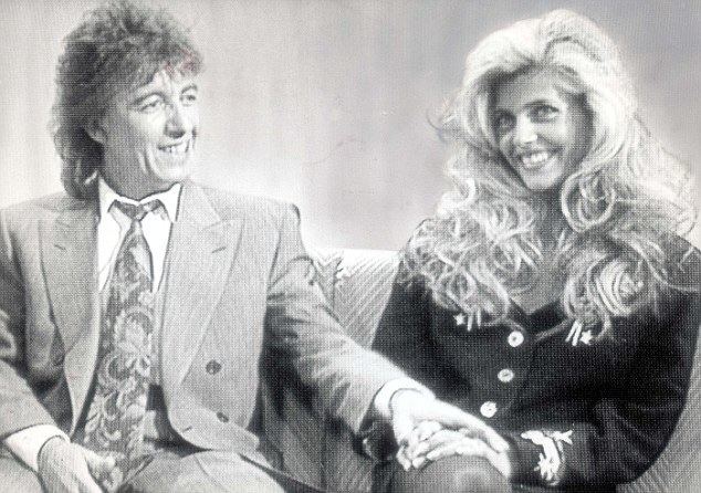 Mandy Smith smiling while Bill Wyman holding her hands and she is wearing a long sleeve blouse
